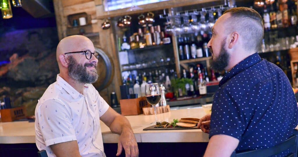 Two guys having a drink at a bar in Eureka Springs, AK, featured in LGBTQ+ travel destination movies.