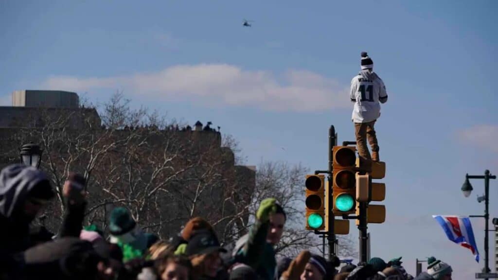 Fans climbing a light pole during the Eagles Super Bowl Parade, surrounded by celebratory chaos.